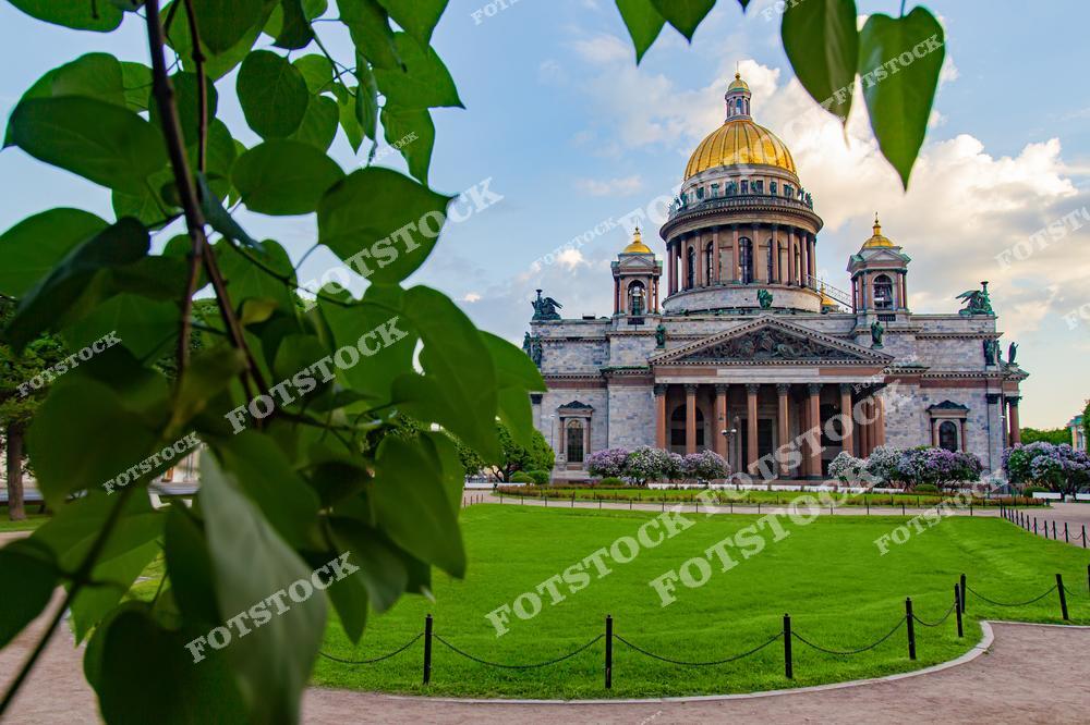 На фотографии запечатлён знаменитый Исаакиевский собор – один из крупнейших православных храмов России. Он расположен на Исаакиевской площади и привлекает внимание своим массивным позолоченным куполом. Внутри собора действует музей, рассказывающий о богатой истории строительства и убранства храма. Летние солнечные лучи подчёркивают красоту монументальных колонн и скульптурных деталей.
